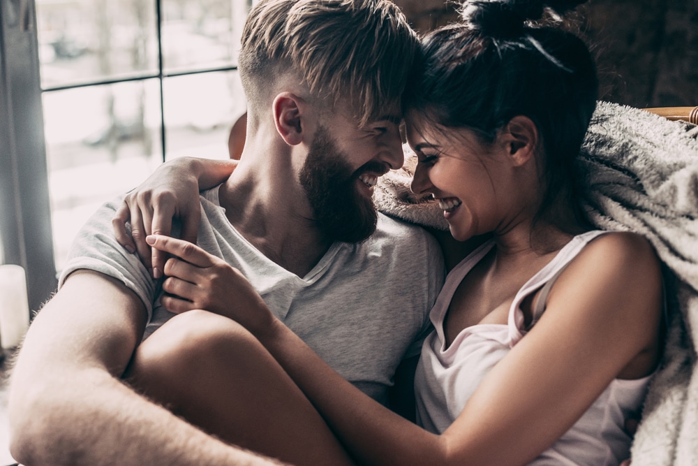 Beautiful young couple smiling and sitting face to face in chair while spending time at home together - Leo Man Qualities