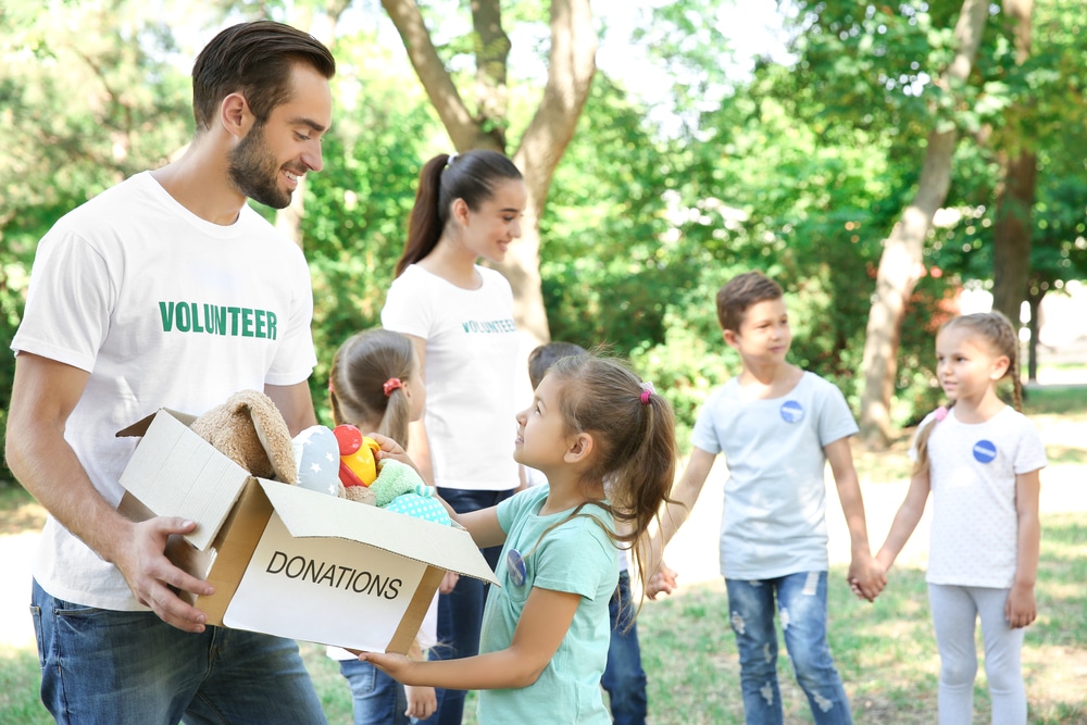 Young volunteers and children with box of donations outdoors - The Leo Man with Pisces Rising