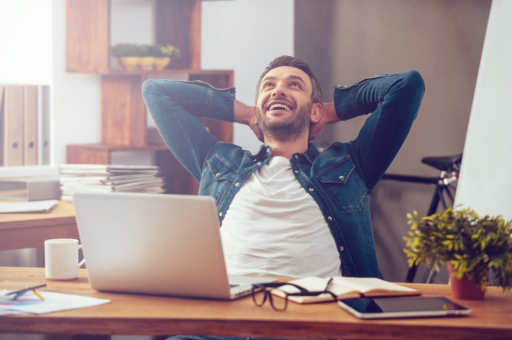 Happy young man working on laptop while sitting at his working place in office - Leo Man With Virgo Rising